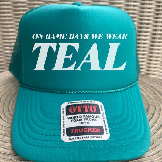 Teal cap with 'On game days we wear teal' text and Otto brand label on a woven surface.