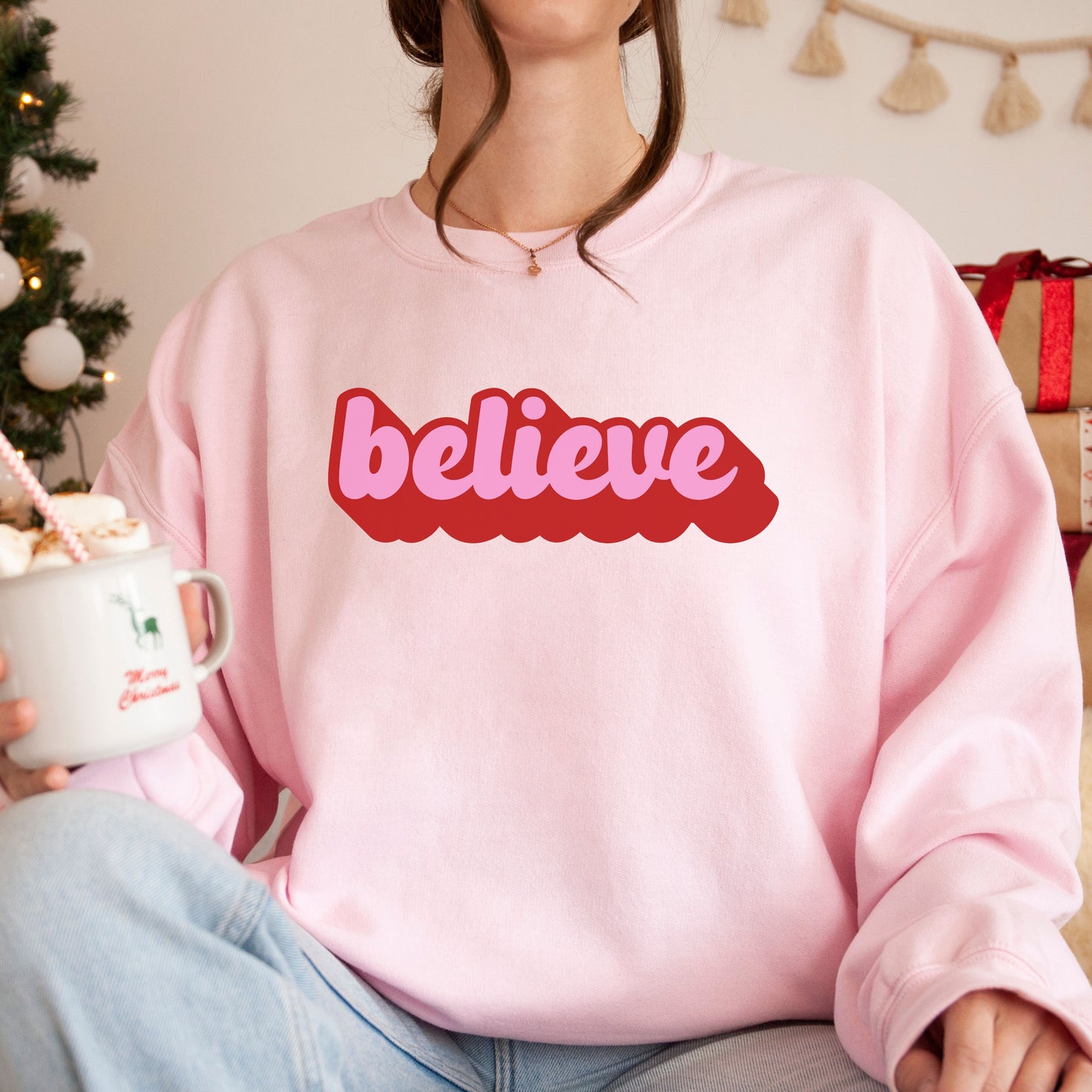 person wearing a pink Christmas sweatshirt with retro "believe" print