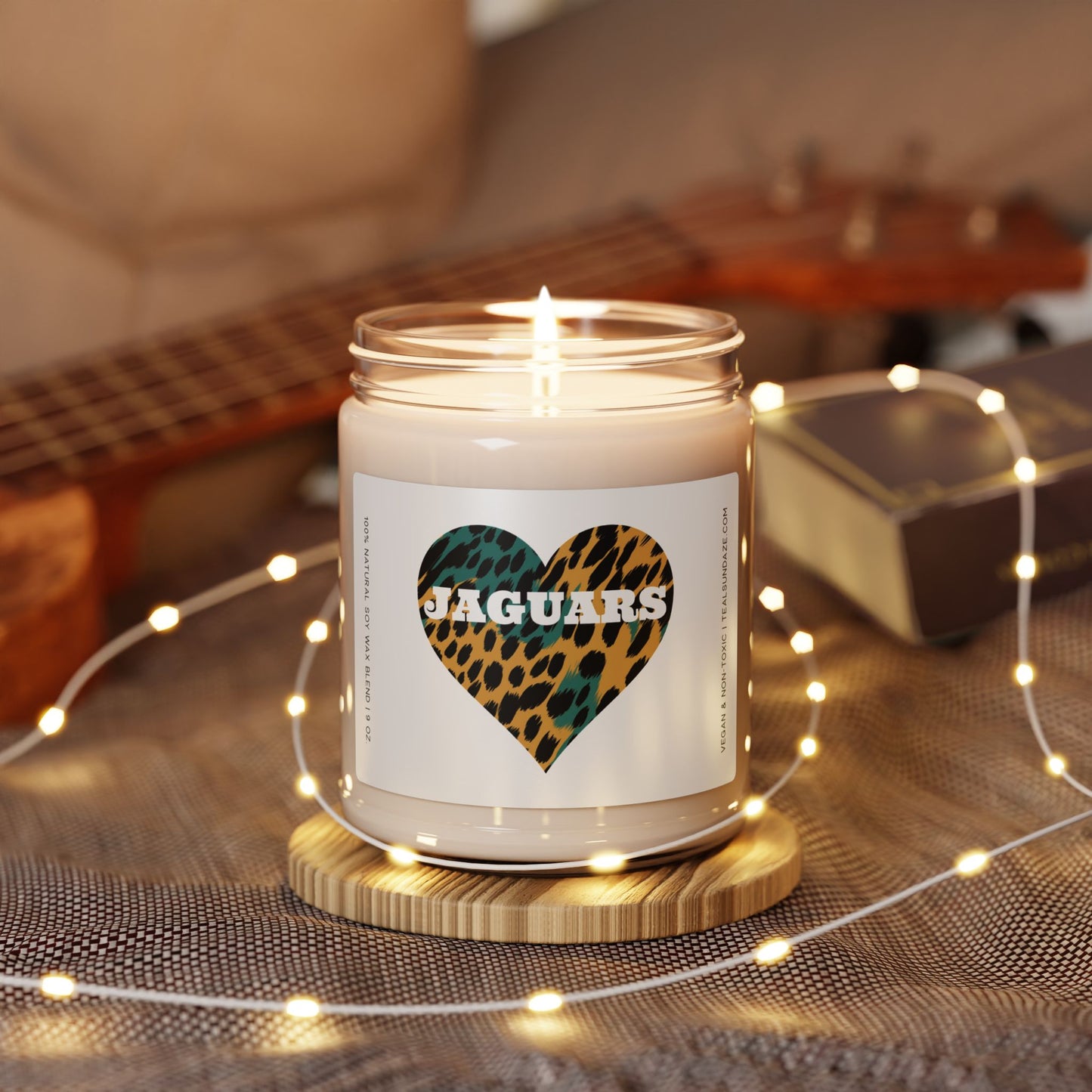 Candle with a 'Jaguars' heart-shaped label on a wooden coaster with string lights and a guitar in the background.