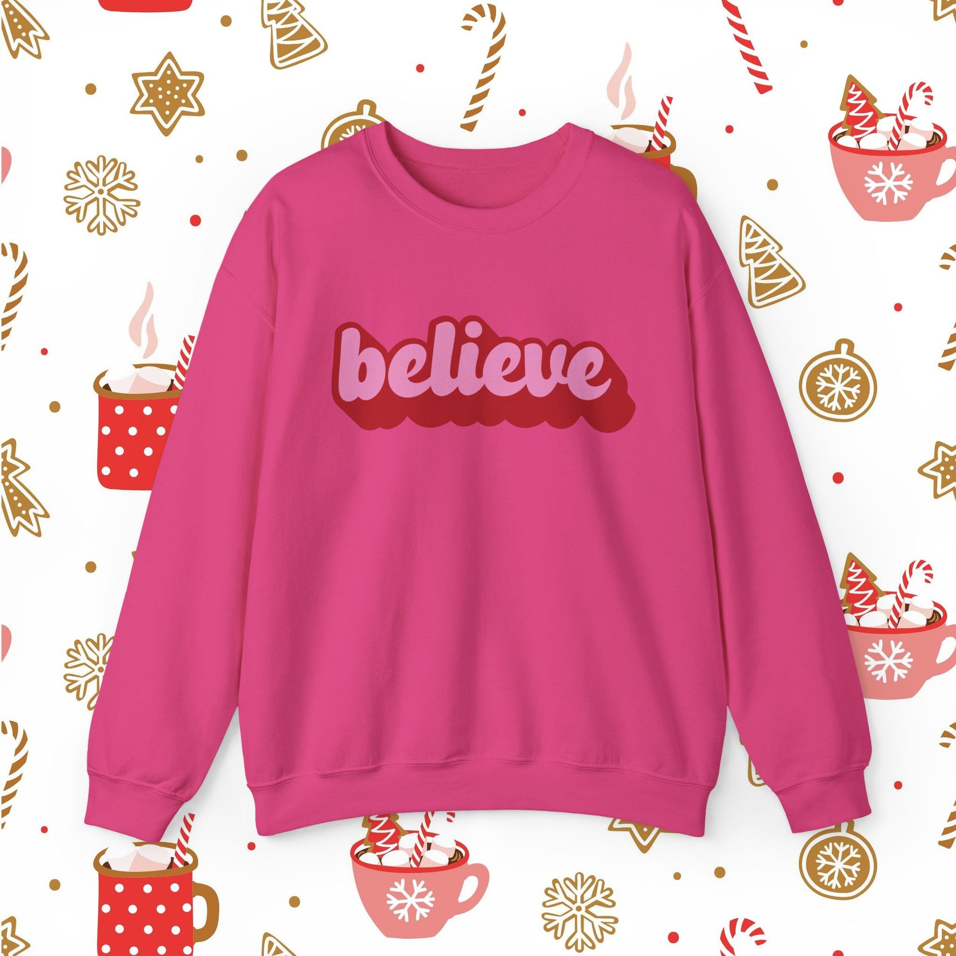 Pink sweatshirt with 'believe' text on a festive background with Christmas elements.