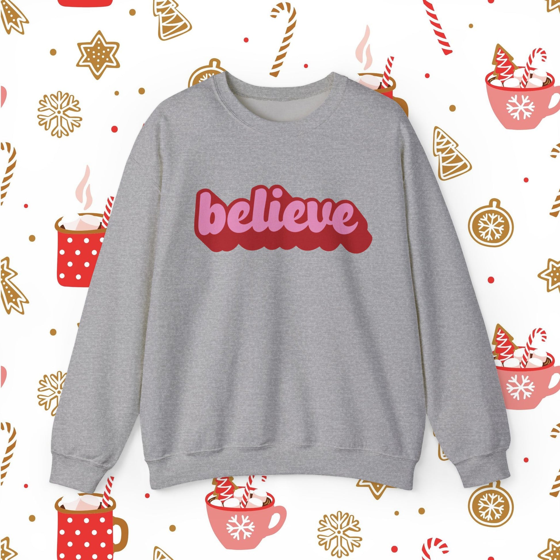 Gray sweatshirt with 'believe' in red on a festive background with hot cocoa and candy cane patterns.