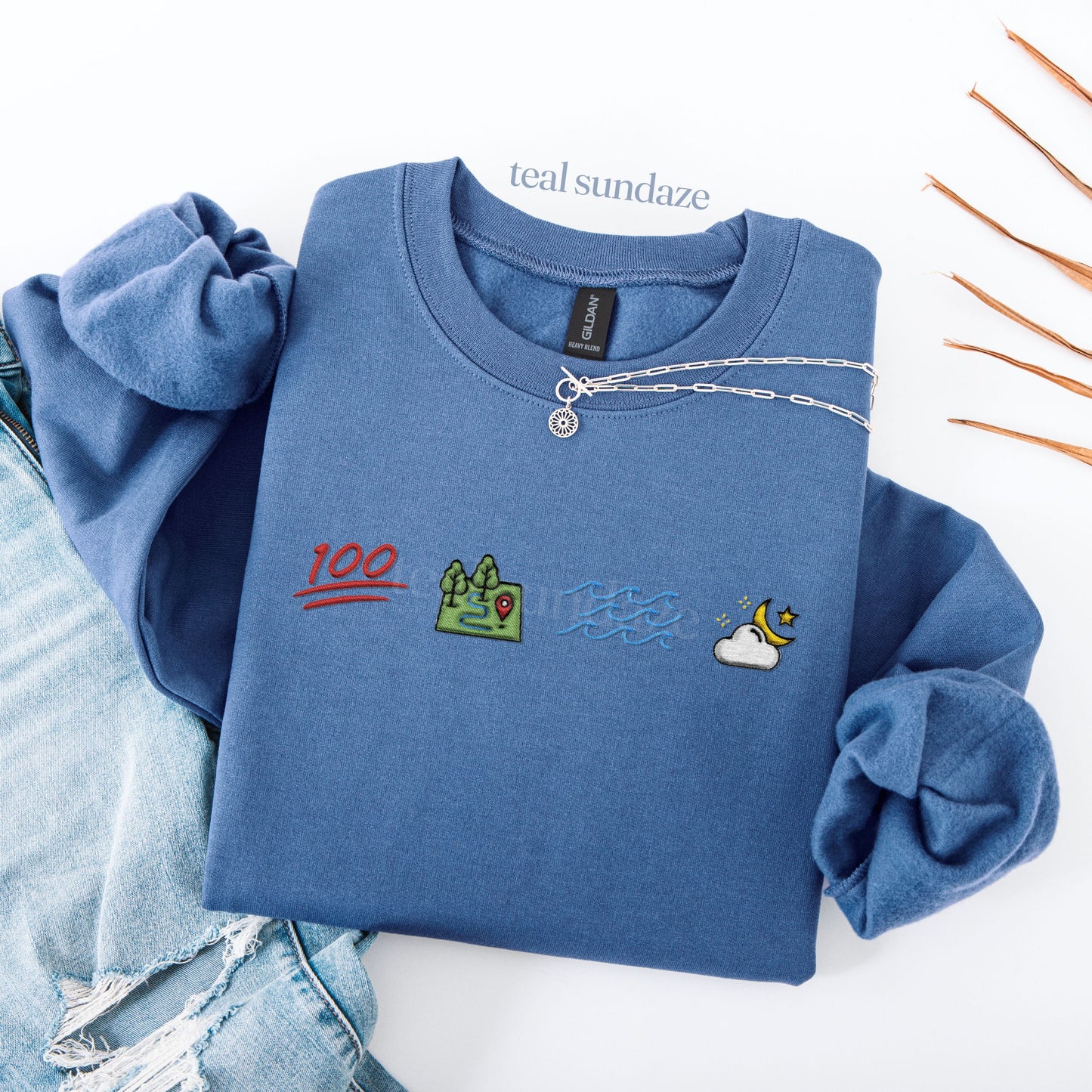 Blue sweatshirt with colorful icons embroidered and 'teal sundaze' branding on a white background