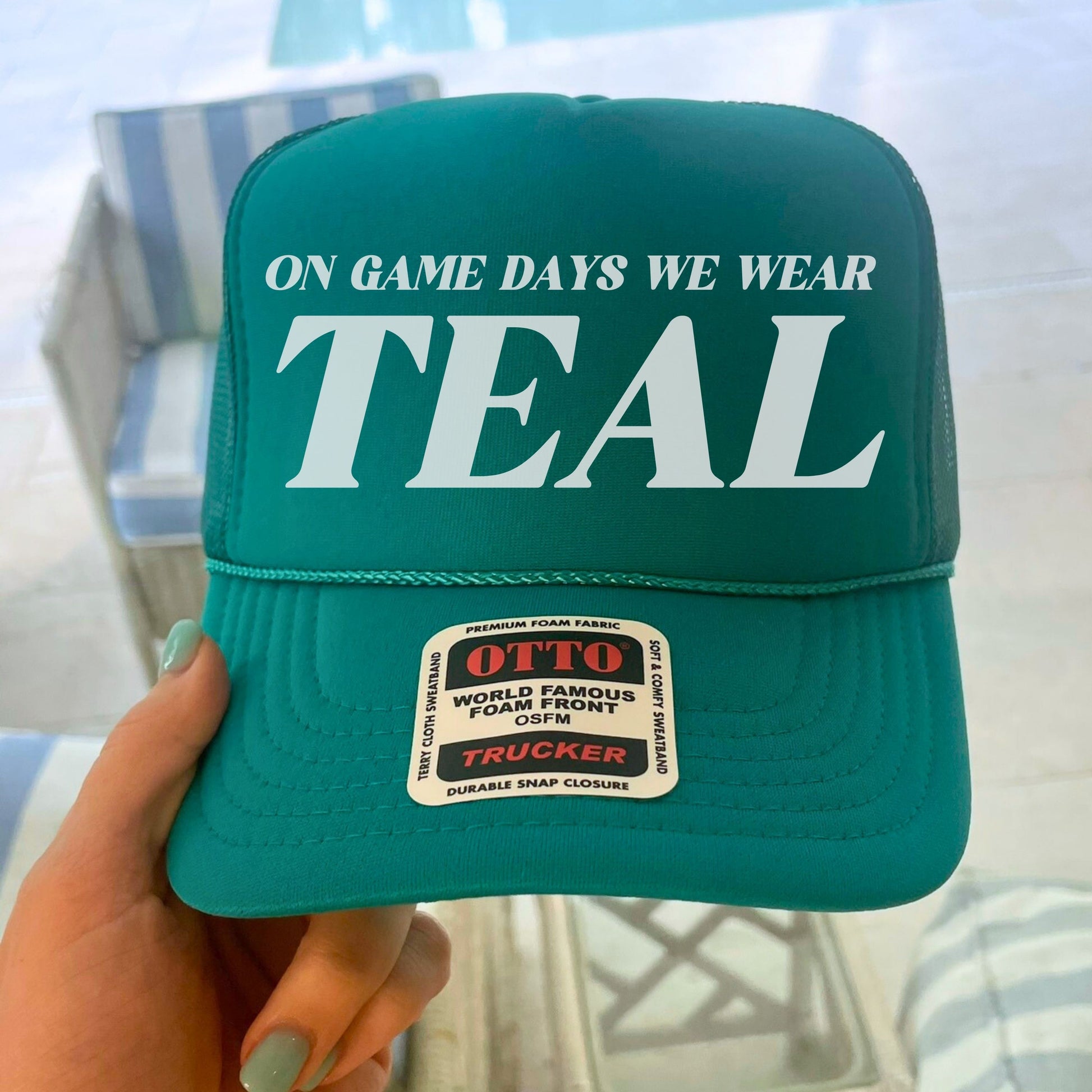 Teal cap with 'ON GAME DAYS WE WEAR TEAL' text, held by a hand.