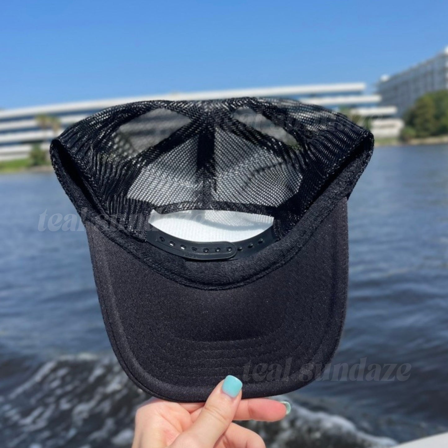 Black mesh cap held in front of a body of water with buildings in the background